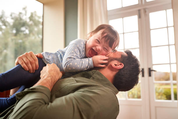 Loving Father Playing With Laughing Down Syndrome Daughter At Home Together stock photo