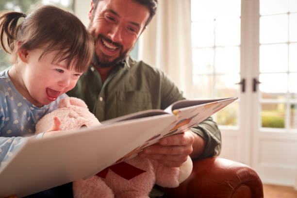 Father With Down Syndrome Daughter Reading Book At Home Together Father With Down Syndrome Daughter Reading Book At Home Together literacy photos stock pictures, royalty-free photos & images