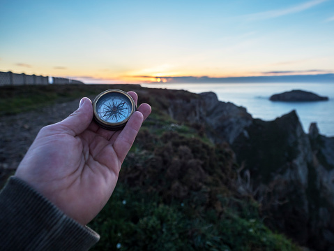 Man's hand holding a compass on a road in a natural environment at sunset. Travel and adventure concept. Horizontal.