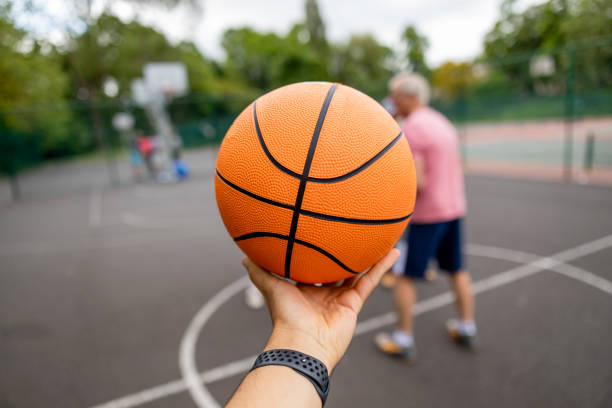 This is My Sport Personal perspective of someone holding and balancing a basketball on their hand with a sports court behind it in Newcastle Upon Tyne, England. Out of focus people can be seen in the background of the shot. asphalt basketball court stock pictures, royalty-free photos & images