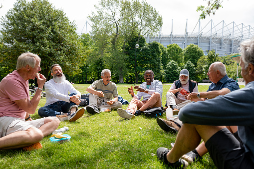 A group of senior men relaxing and enjoying a day out in the park together in Newcastle Upon Tyne, England. They are having a picnic together while sitting on the grass and laughing.
