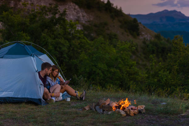 istock Young couple drinking coffee, enjoying the mountain view and checking the tablet with bonfire in the sunset 1387464582