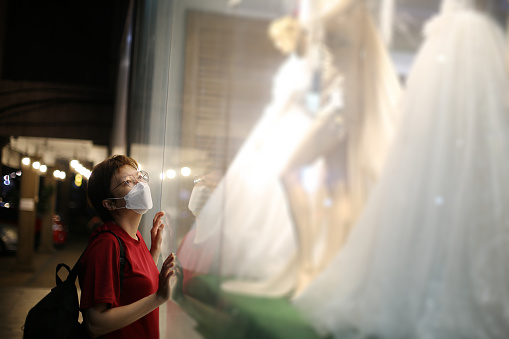 An Asian woman is admiring bridal gown at bridal boutique display.