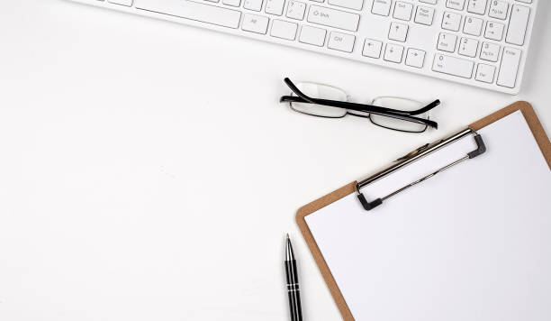 istock Directly above view of table, pen, papers and computer keyboard on the white background 1387472126