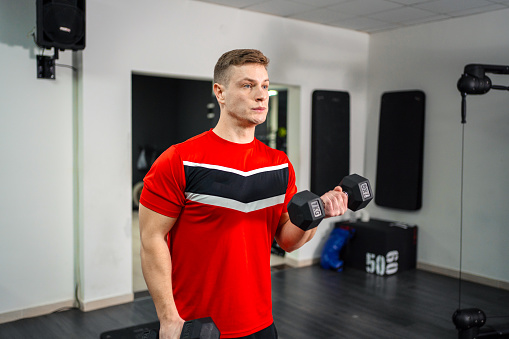 Athletic young man training biceps in the gym