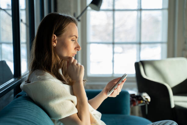 istock Serious excited young woman exchanges text messages using a mobile phone while sitting at home on the couch 1387475681