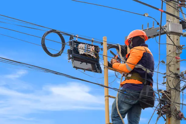 Photo of Technician on wooden ladder using smartphone to check data numbers of cable lines while installing fiber optic system in internet splitter box on electric pole