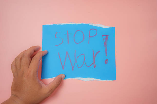 istock Man's hand holding a blue paper with the text stop war on a pink background No war, stop war, russian aggression. 1387479475