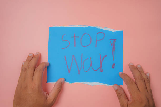 istock Man's hand holding a blue paper with the text stop war on a pink background No war, stop war, russian aggression. 1387479534