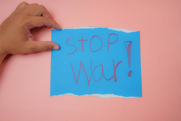 istock Man's hand holding a blue paper with the text stop war on a pink background No war, stop war, russian aggression. 1387479550