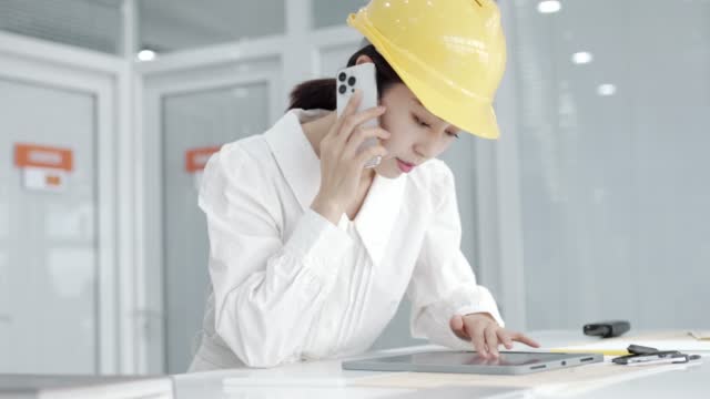 Beautiful young asian  female engineer in yellow helmet and using tablet design