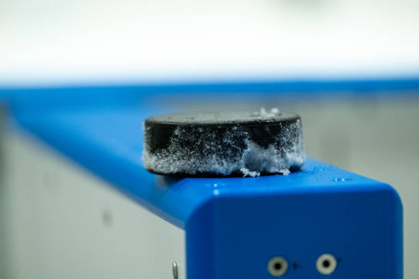 Closeup of a snow covered ice hockey puck standing on the side of an ice hockey rink. stock photo