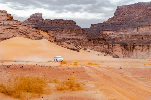 Djanet, Illizi. Algeria - December 22, 2021: Sahara Desert sand dune, dry herbs and rocky mountain. Tadrart Rouge,  Orange colored sandstones. Blue cloudy sky