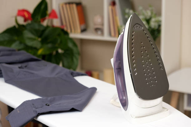 istock Iron on a white ironing board and a gray men's shirt. 1387483569