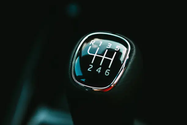 Close up color image depicting the top side of a gear stick (or stick shift) in a car interior. Focus is on the gear stick while the background is blurred pleasantly out of focus. Room for copy space.