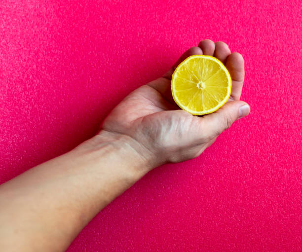 istock Hand holding lemon cut in half on bright pink background. Food 1387487076