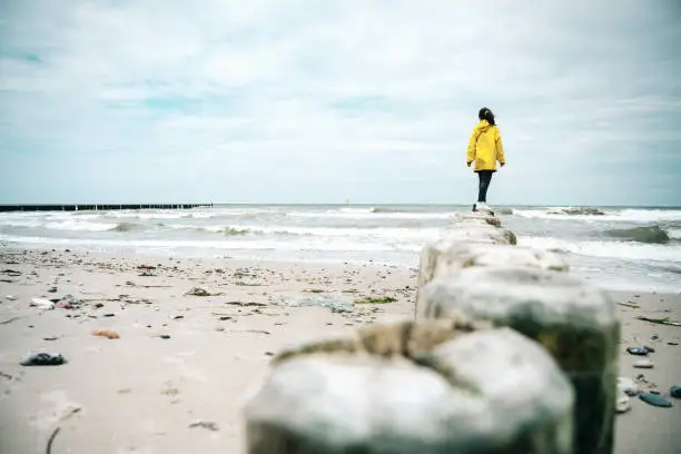 rear view on little girl in yellow raincoat balancing on groyne at beach of baltic sea