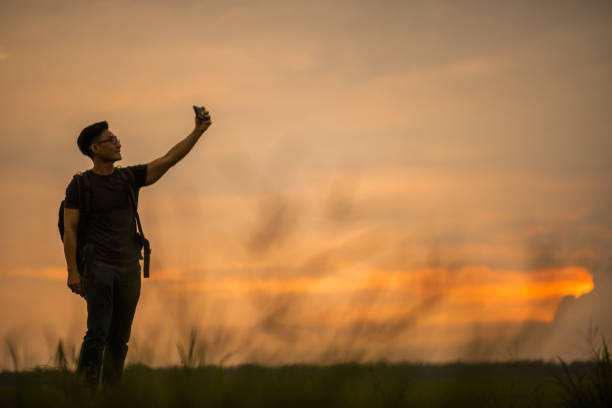 Asian Chinese backpacker man taking photo in paddy field sunset time. stock photo