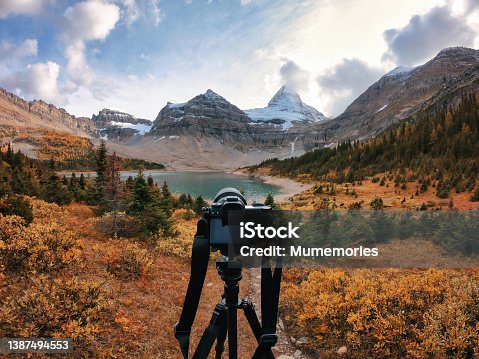 istock Mirrorless camera on tripod standing in autumn forest with mount Assiniboine in national park 1387494553
