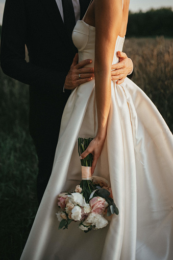 Groom in a blue checkered suit hugs bride in a white dress with a bouquet of flowers. Close-up. High quality photo