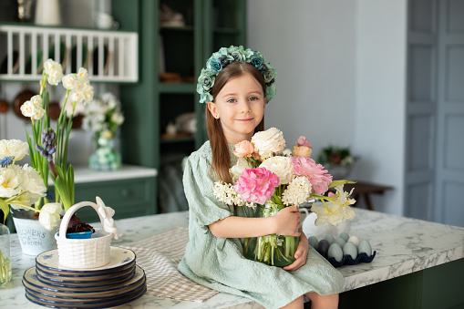 Girl and flower. Spring holiday. Womens day. happy little girl in dress with long hair holding bouquet flowers. Childhood. Celebration, mothers day. Child with flowers in glass vase in Easter kitchen