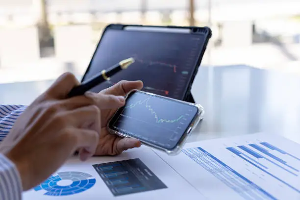 Photo of An investor is looking at stock charts on mobile phones and tablets, he is a stock investor, he trades stocks by analyzing the charts and using indicators to enter trades. Stock investment idea.