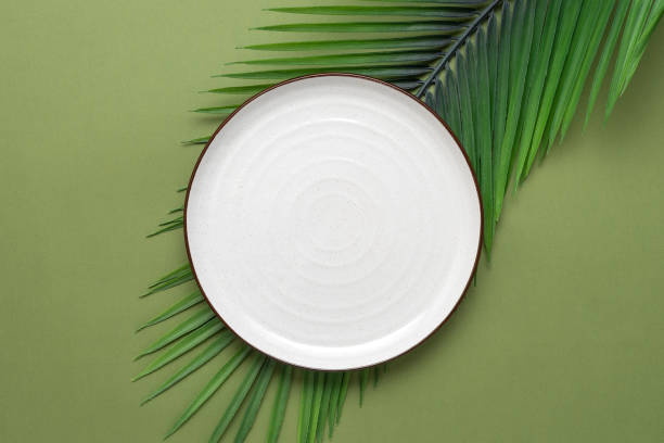 istock Empty white plate and decorative palm leaves on olive green background. Top view, flat lay. 1387500996