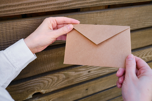 Woman holds in hand paper envelope. New mail, message. Postal service. Young girl want send or receive letter. Blank envelope, empty space. People communication concept. Envelope mockup closeup