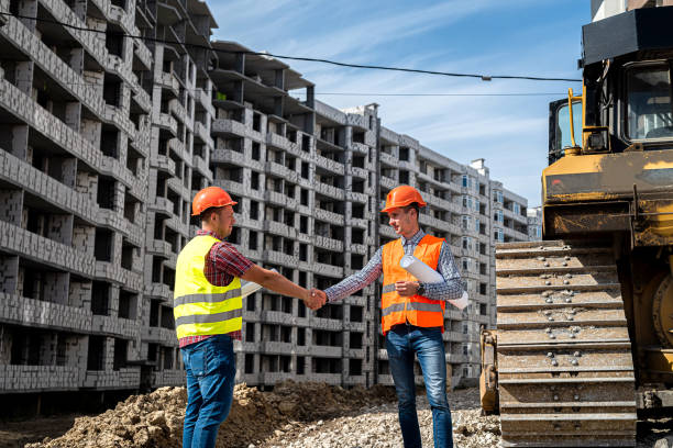 istock two good workers in uniform shake hands near the grader and the new building 1387504974