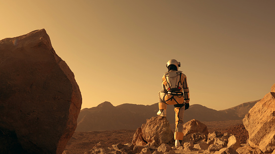 Red dirt on Mars surface. Woman wearing futuristic exoskeleton exploring cave and mountain areas