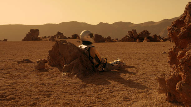 istock Loneliness on Mars. Female astronaut exploring rust colored caves and rocks. Sitting on a rock 1387508729