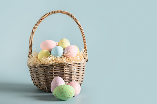 Easter wicker basket with pastel colorful eggs for festive holiday on blue background. Greeting card with copy space.