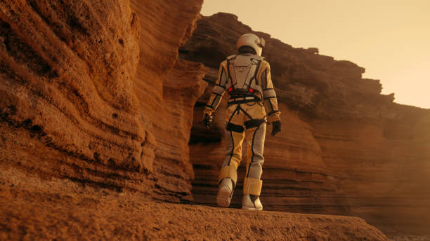 istock Loneliness on Mars. Female astronaut exploring rust colored caves and rocks. Touching stone walls 1387509039