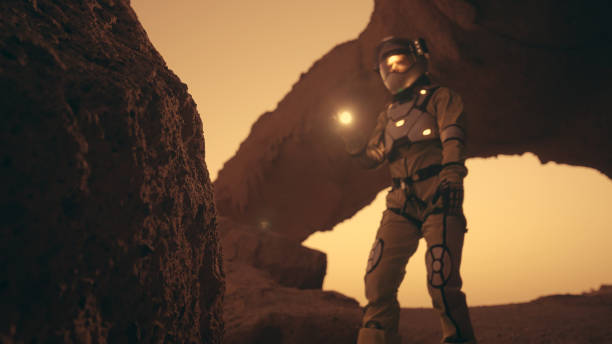 istock Loneliness on Mars. Female astronaut exploring rust colored caves and rocks. Touching stone walls 1387509174
