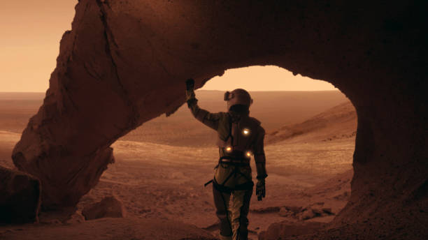 istock Loneliness on Mars. Female astronaut exploring rust colored caves and rocks. Touching stone walls 1387509175