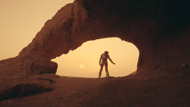 istock Loneliness on Mars. Female astronaut exploring rust colored caves and rocks. Touching stone walls 1387509268