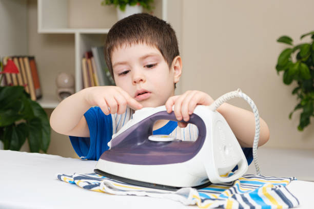 A boy of 4 years learns to hold an iron, iron clothes on an ironing board.