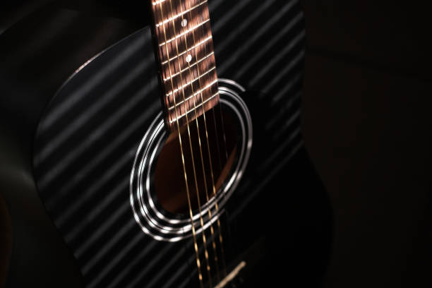 Black guitar on a dark background in a light-shadow pattern from the blinds