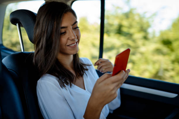 istock Smiling young woman using phone in car 1387512744