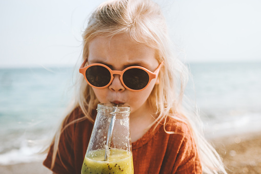 Child drinking smoothie on beach  summer vacations breakfast healthy eating lifestyle vegan food girl with glass bottle and sunglasses