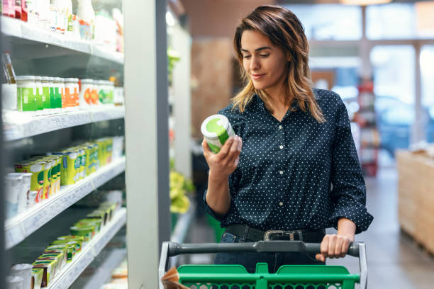 donna di bellezza che cammina con il carrello della spesa mentre prende i prodotti dallo scaffale al supermercato - organic spices foto e immagini stock