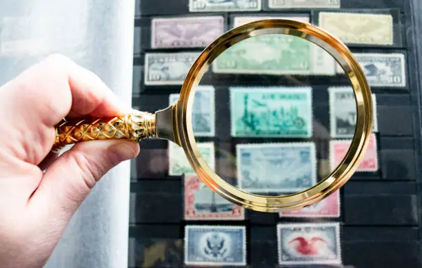 Moscow, Russia, March 2022: Hobby: stamp collecting. Looking at blurred old stamps through a golden magnifying glass. Copy space.
