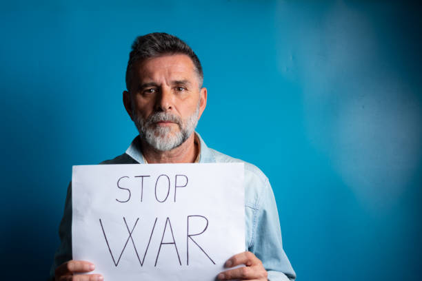 istock Text message stop war. Mature bearded man with an anxious, fearful expression, with stop war banner in Hand. Bearded senior man with an anxious, fearful expression. 1387519223