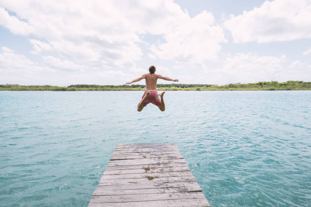 istock Happy young man jumping from pier into beautiful lake 1387520676