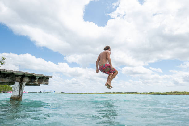 istock Happy young man jumping from pier into beautiful lake 1387520764