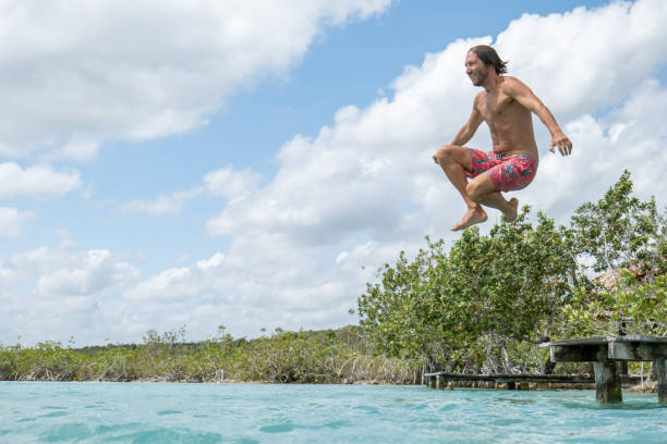 istock Happy young man jumping from pier into beautiful lake 1387520798