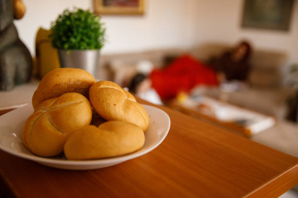 Selective focus shot of delicious buns served on the plate, sitting on the kitchen counter. In the background, mother and daughter casually lounging in the living room. Focus on foreground.