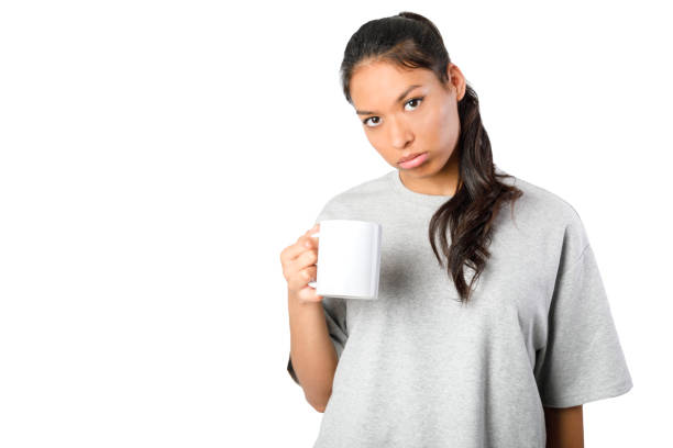 Sleepy woman holding a mug. Tired woman, looking at camera. Isolated on white background. Young asiatic woman.