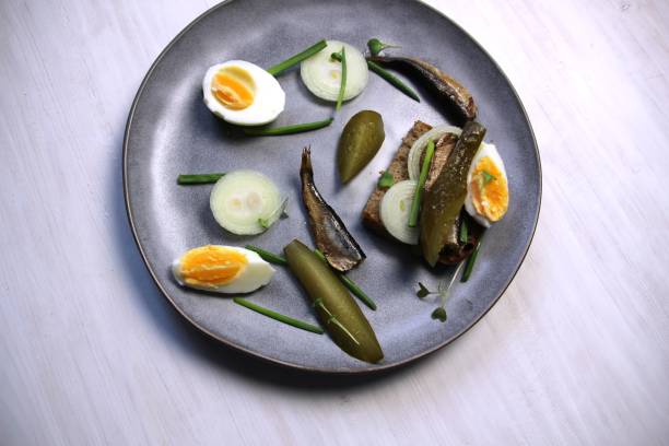 istock Plate with open sndwich with sprats, salty cucumber, onion, scallion, egg, bread on white background 1387528124