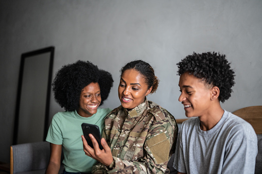 Soldier mother using the mobile phone with son and daughter at home